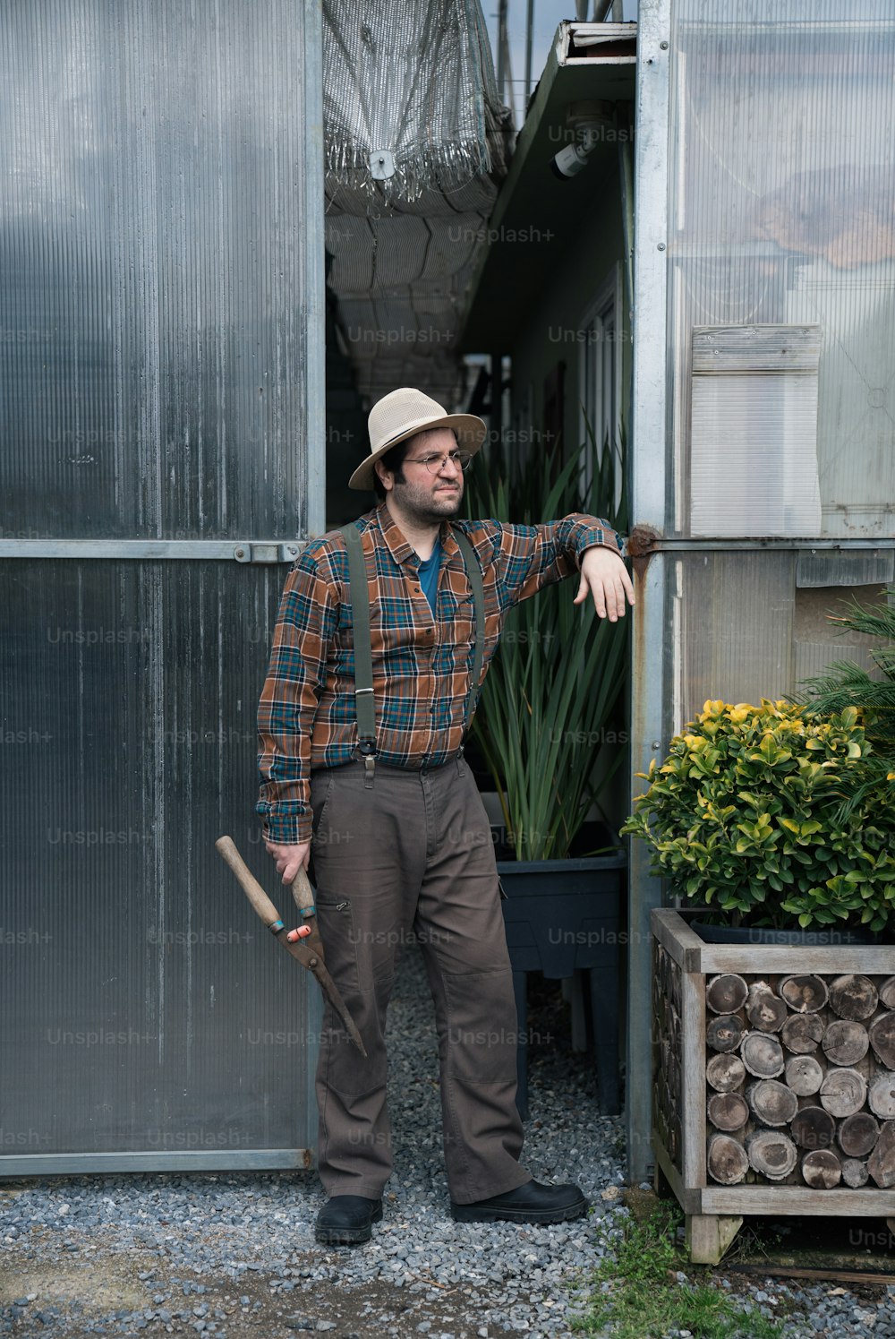 温室の前に立つ帽子とオーバーオールを�着た男