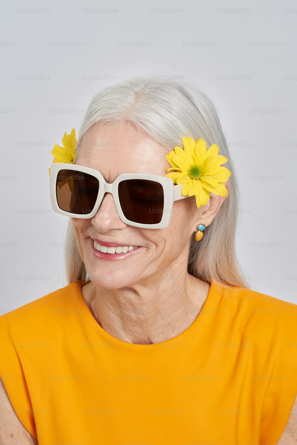 Una donna anziana che porta occhiali da sole e un fiore tra i capelli