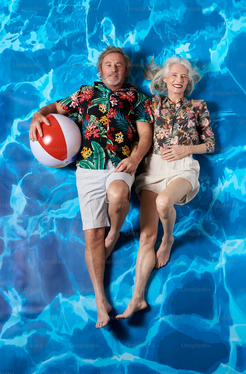 a man and a woman laying in a pool with a ball