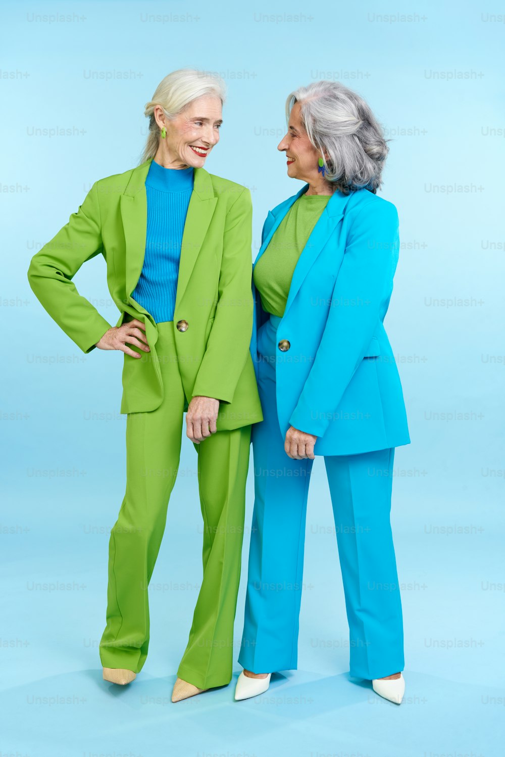 two women standing next to each other in green and blue outfits