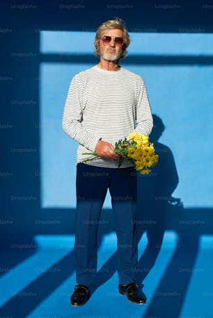 a man standing in front of a blue wall holding a bouquet of flowers