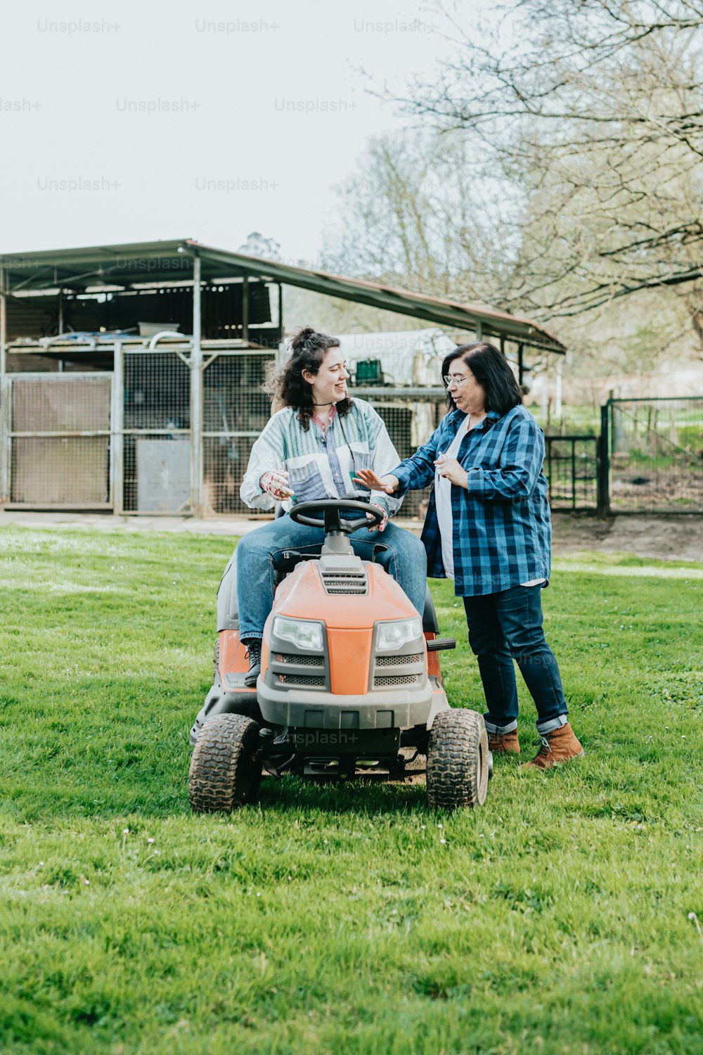 a couple of women sitting on top of a lawn mower
