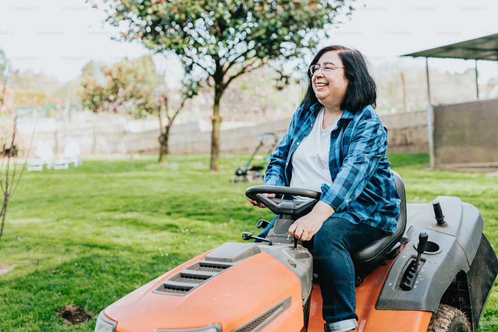 a woman riding on the back of an orange lawn mower