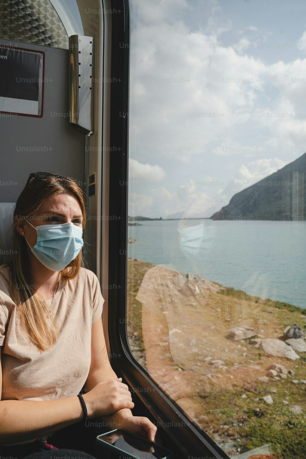 フェイスマスクをかぶった女性が電車の窓の外を見ている