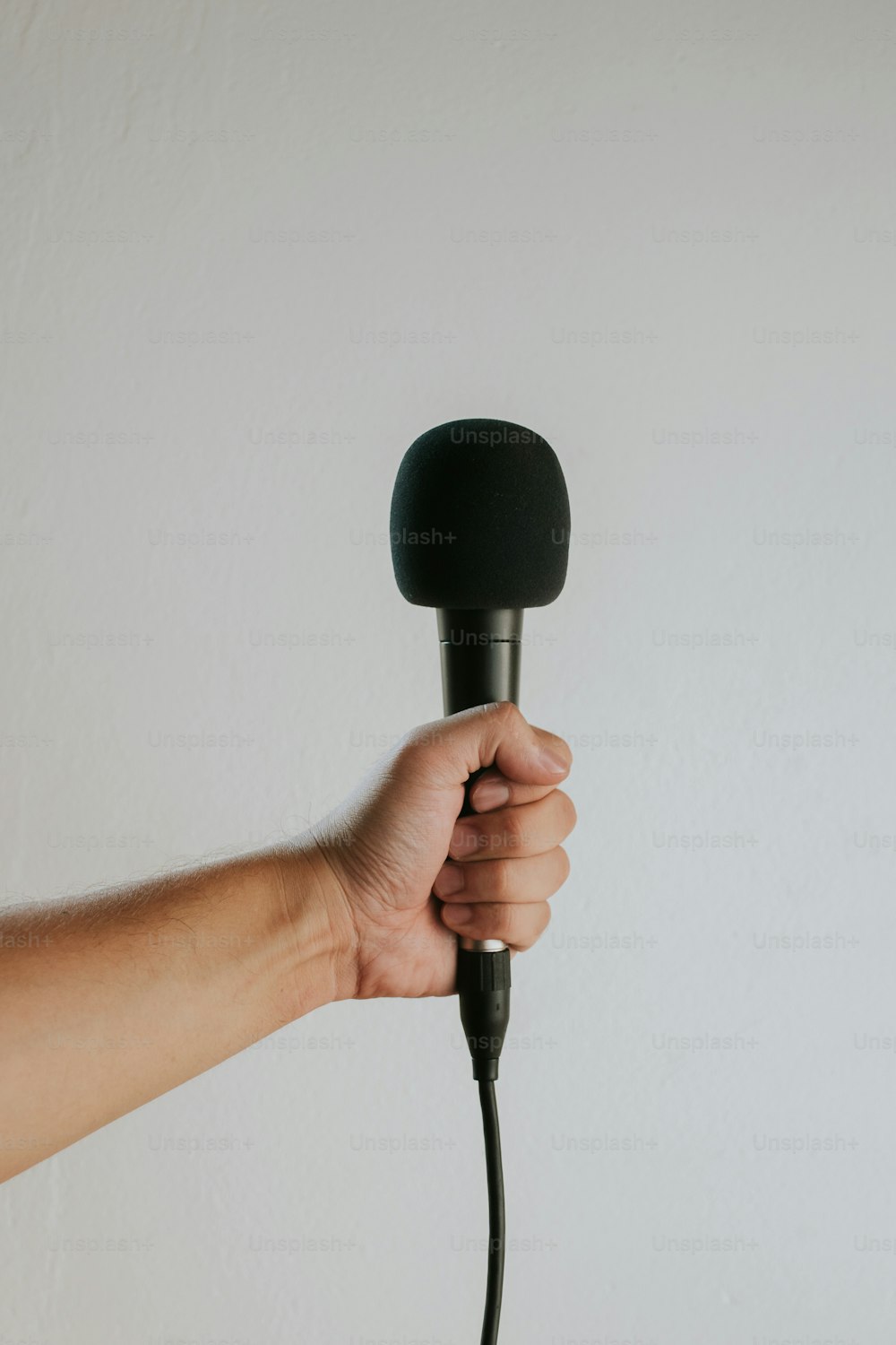 a hand holding a microphone over a white wall