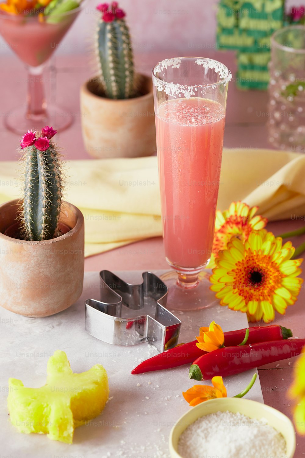 a table topped with a glass of pink liquid next to a cactus
