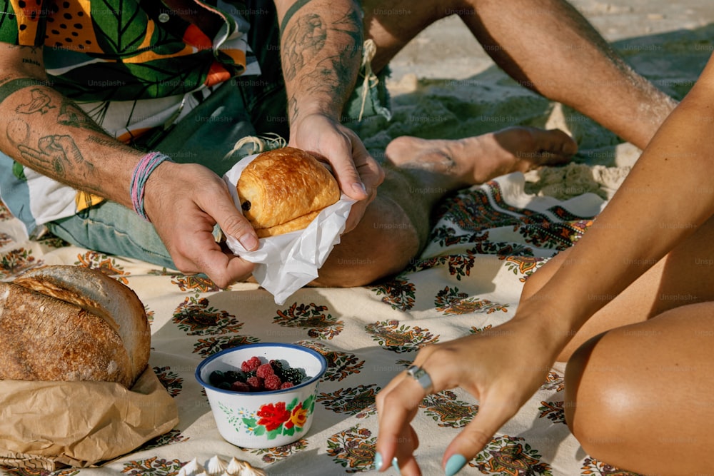 um homem e uma mulher sentados na praia comendo um sanduíche