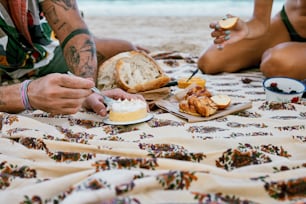 um casal de pessoas sentadas em uma praia comendo comida