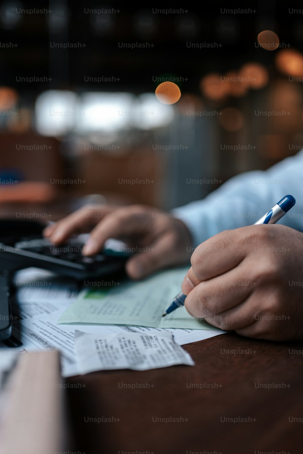 eine Person, die mit einem Taschenrechner und einem Stift an einem Schreibtisch sitzt