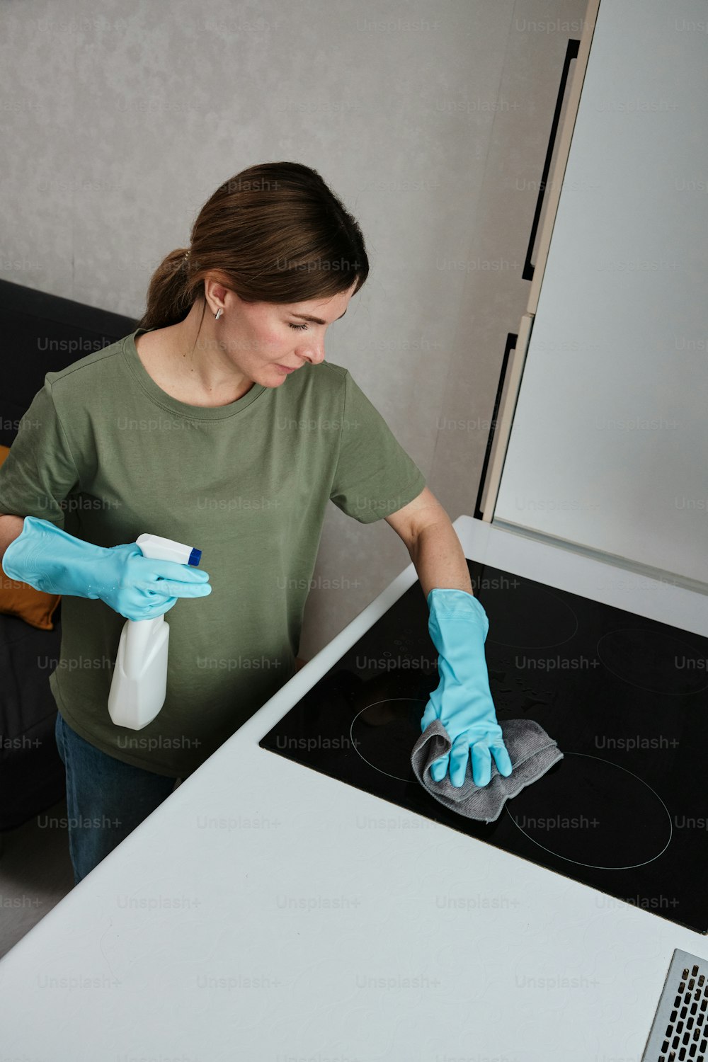 a woman in a green shirt and blue gloves cleaning a stove