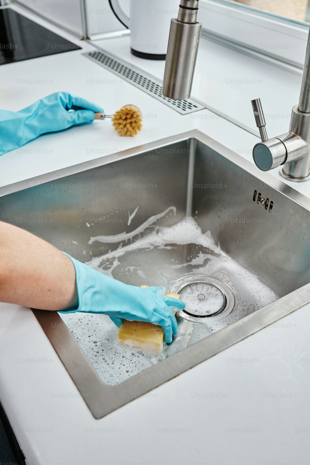 Eine Person in blauen Handschuhen reinigt ein Waschbecken aus Edelstahl