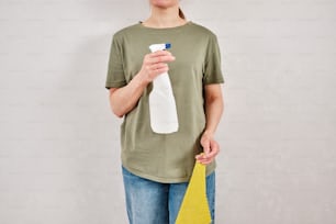 uma mulher segurando uma garrafa de limpador e uma esponja