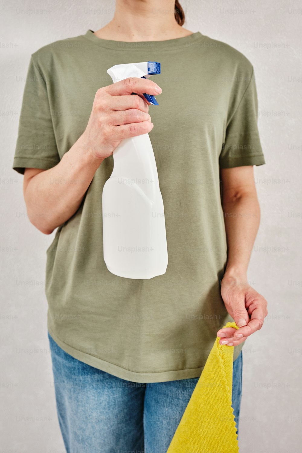 a woman holding a bottle of cleaner and a sponge
