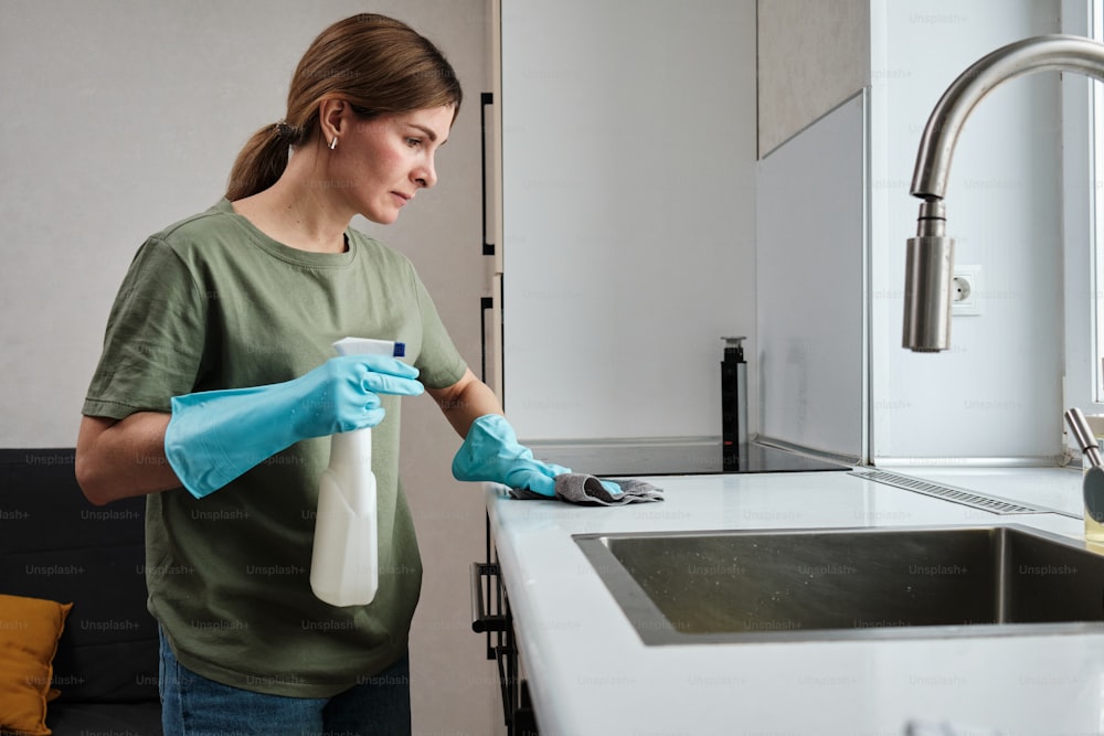 Una donna con una camicia verde e guanti blu sta pulendo un lavandino