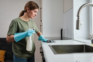 a woman in a green shirt and blue gloves is cleaning a sink