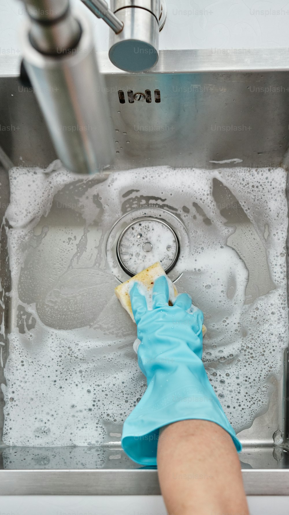 a person cleaning a sink with a blue glove