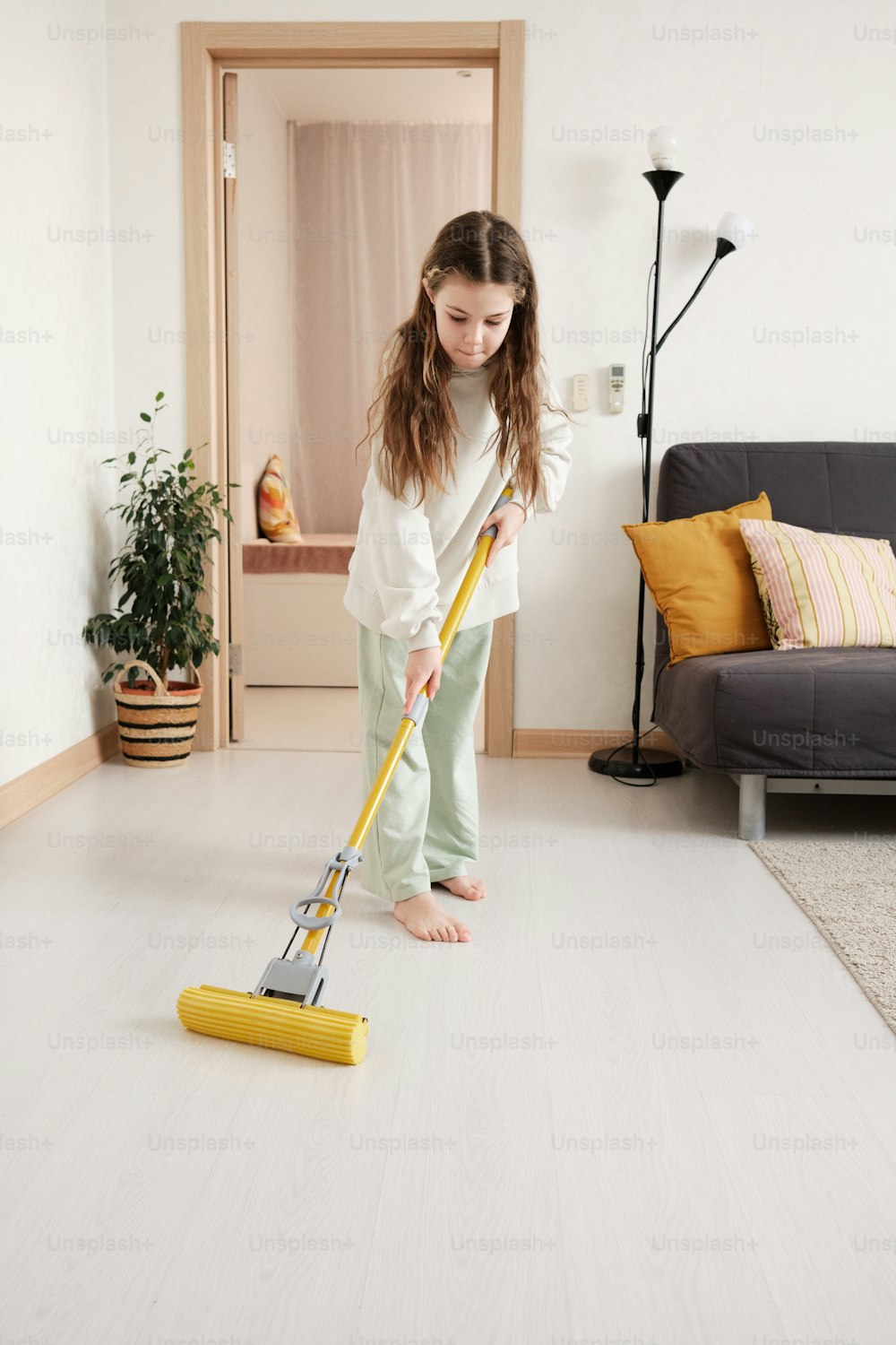 a young girl is cleaning the floor with a mop