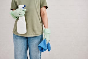 a person in a green shirt holding a blue cloth and a bottle of cleaner