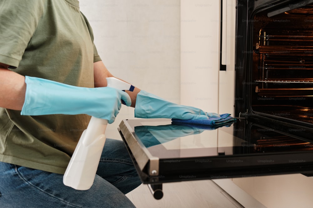 a person in blue gloves cleaning an oven
