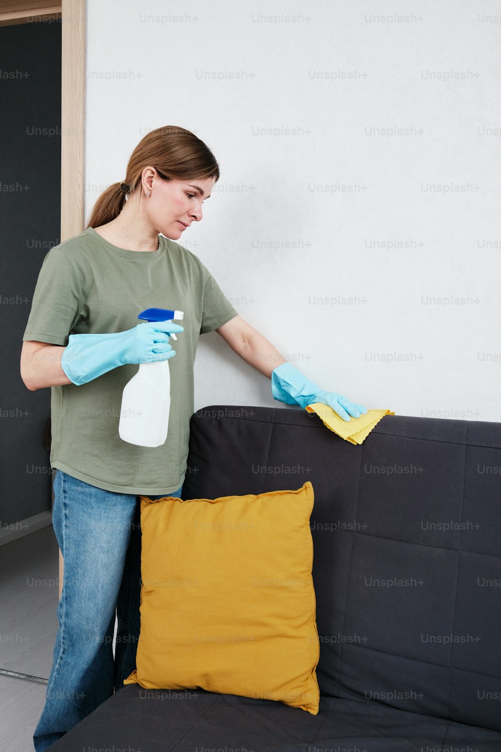 Una mujer limpiando un sofá negro con una almohada amarilla
