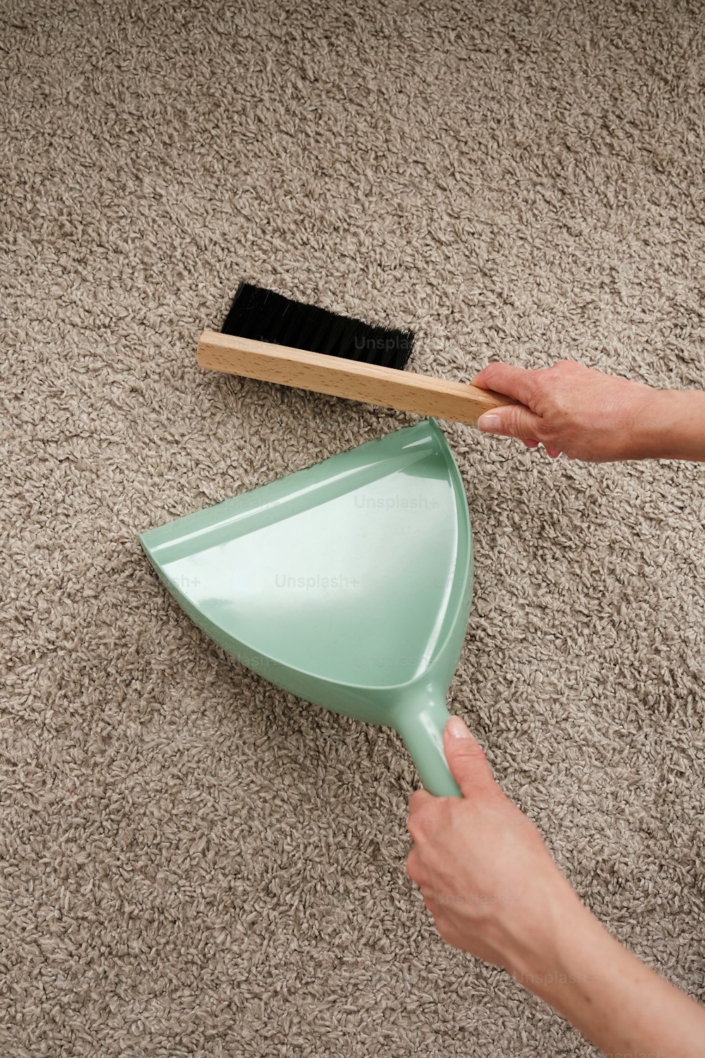 uma pessoa segurando uma lixeira e uma escova de poeira em um tapete