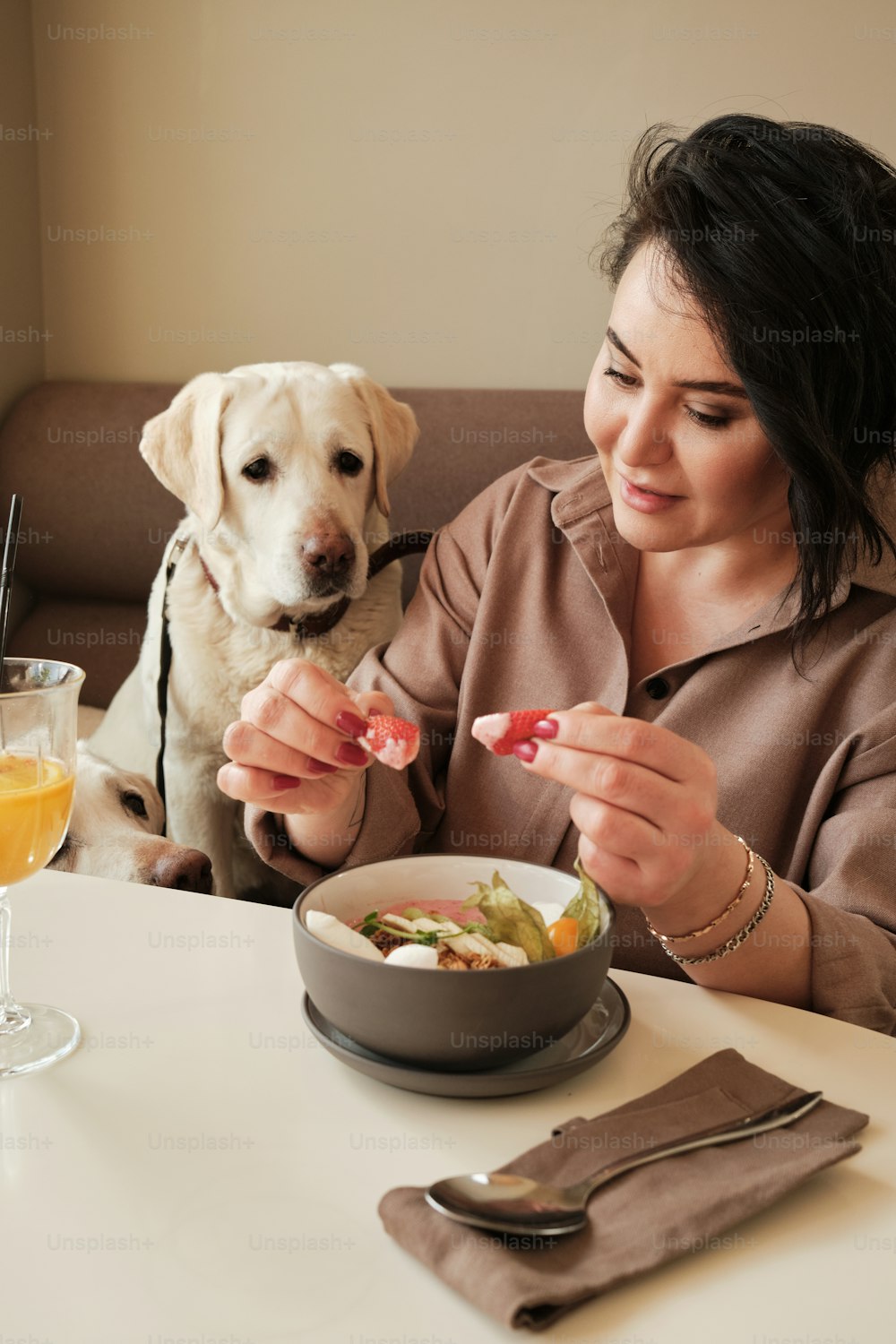 a woman sitting at a table with a bowl of food and a dog