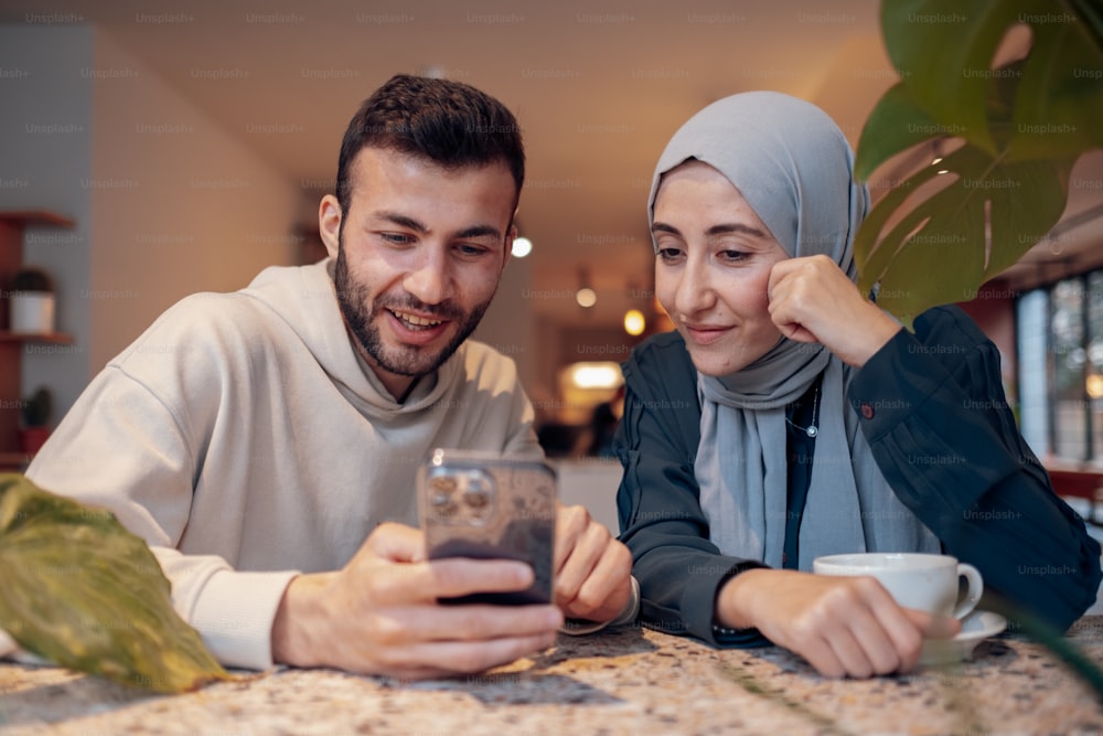 Un hombre y una mujer sentados en una mesa mirando un teléfono celular