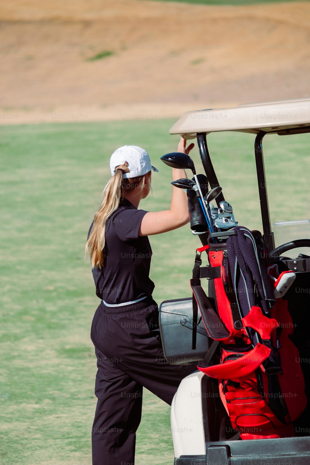 a woman putting golf equipment in the back of a golf cart