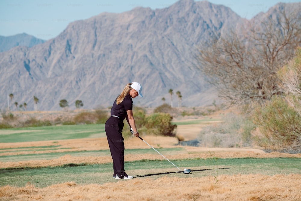 a woman playing golf in the desert with mountains in the background