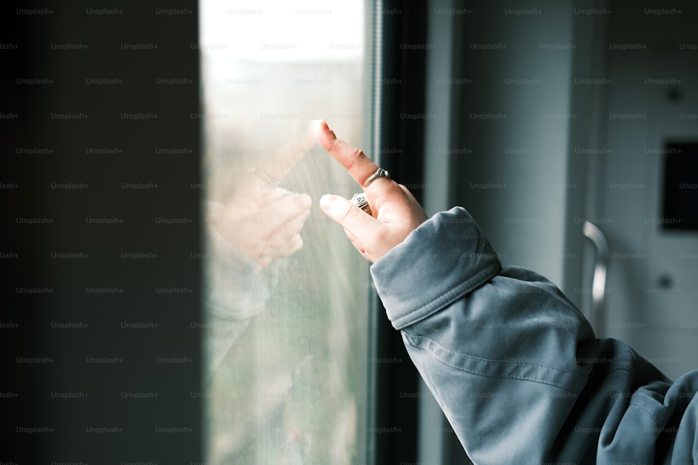 uma pessoa em pé na frente de uma janela segurando um telefone celular