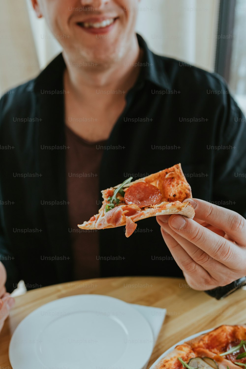 um homem sentado em uma mesa com uma fatia de pizza na mão