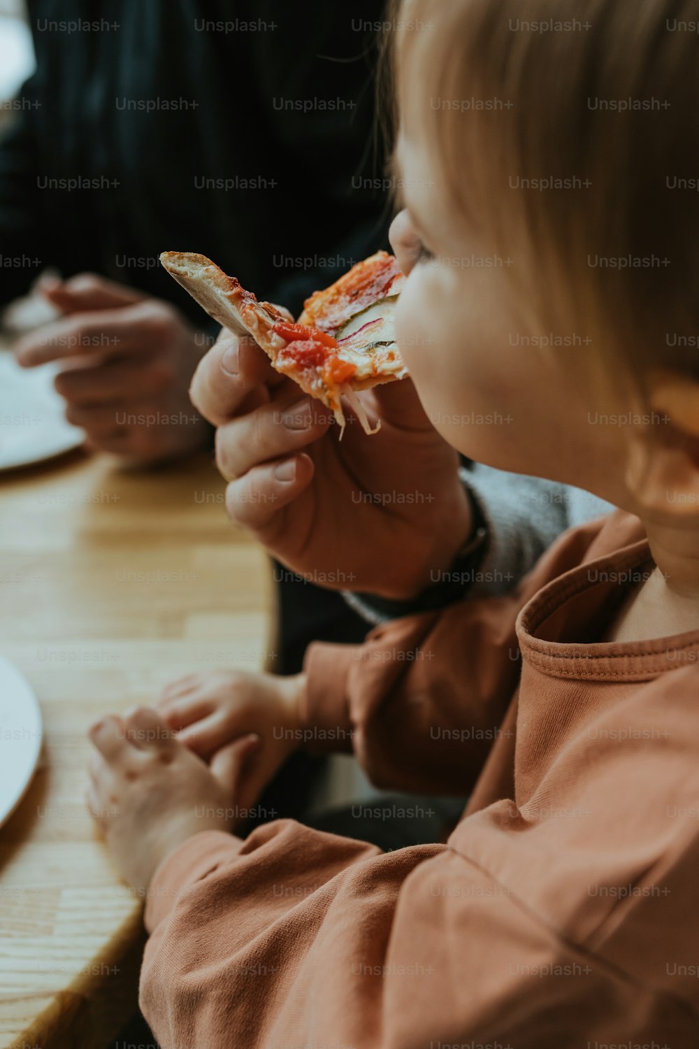 Un petit garçon assis à une table mangeant une part de pizza