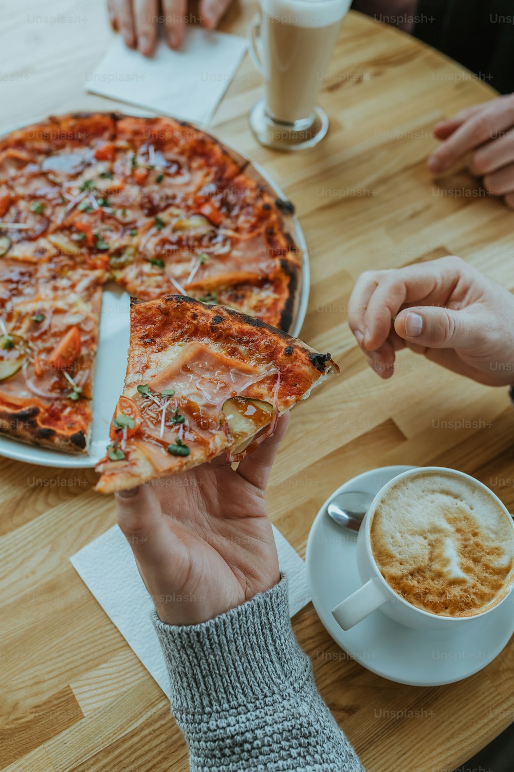a person holding a slice of pizza in front of a cup of coffee