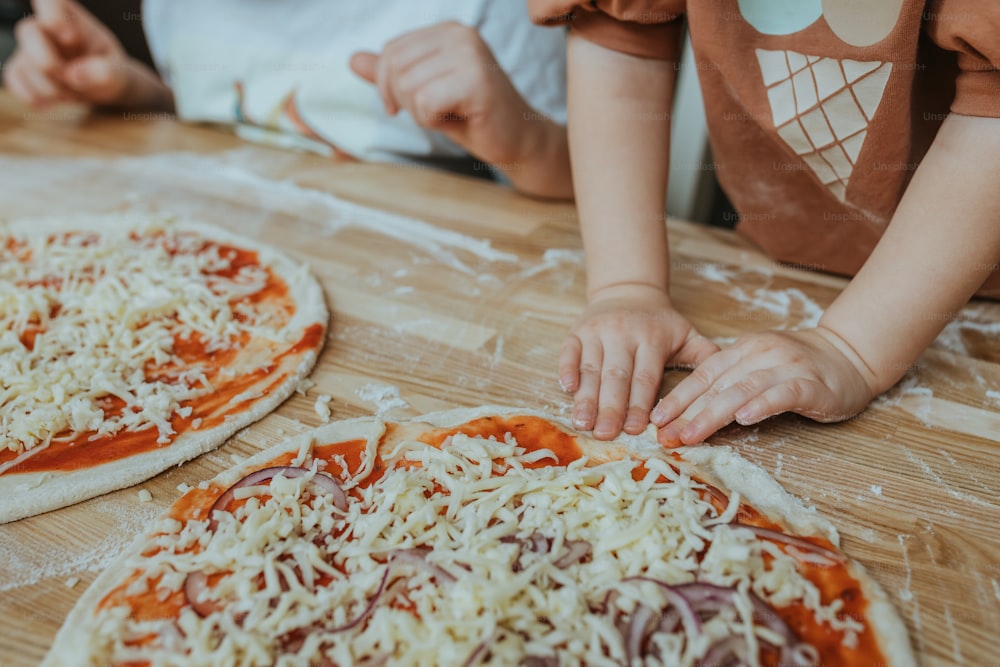 two children are making homemade pizzas on a table