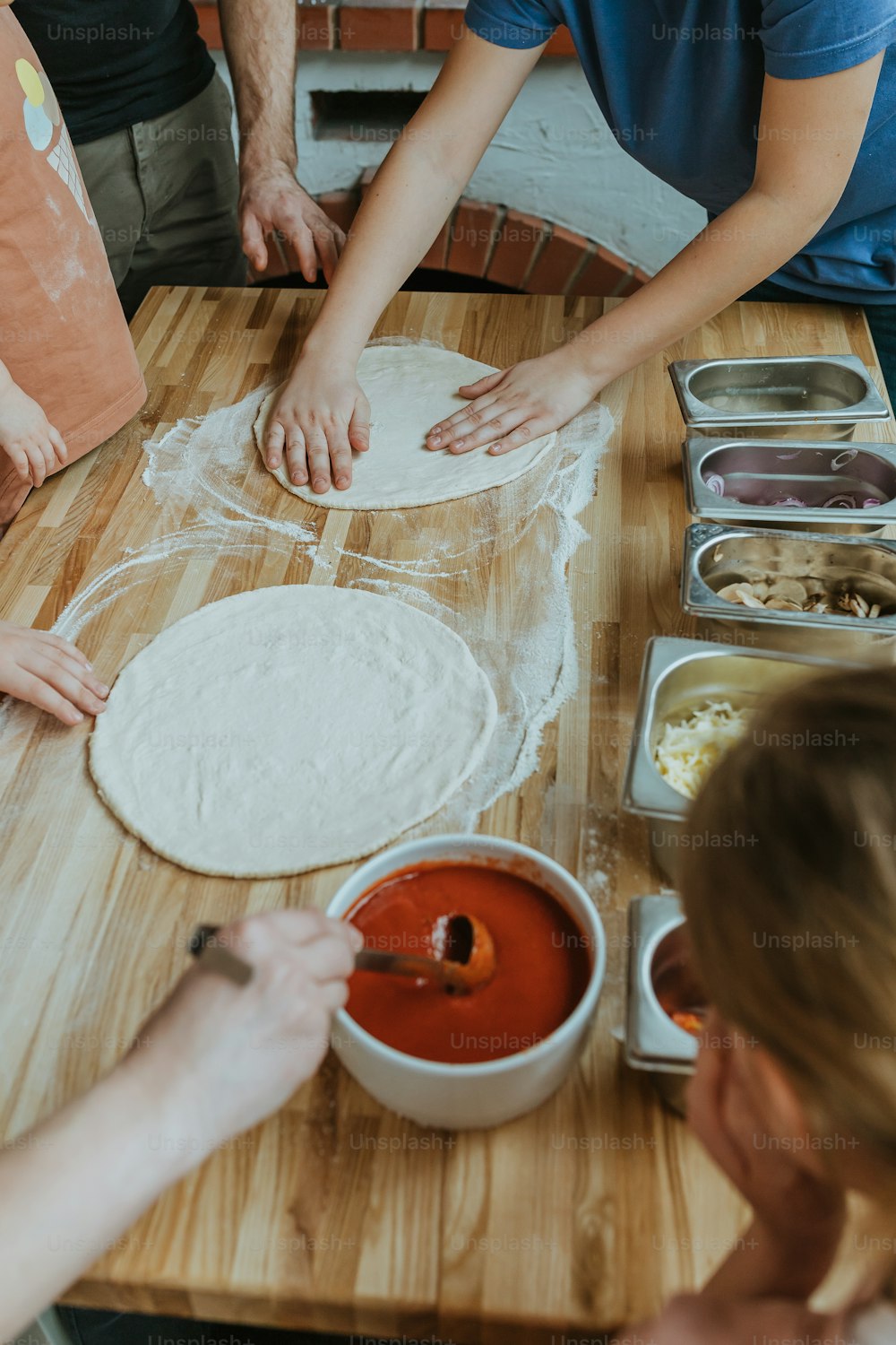 a group of people making pizza dough on a wooden table