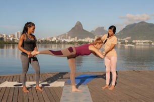 three women doing yoga on a dock near a body of water