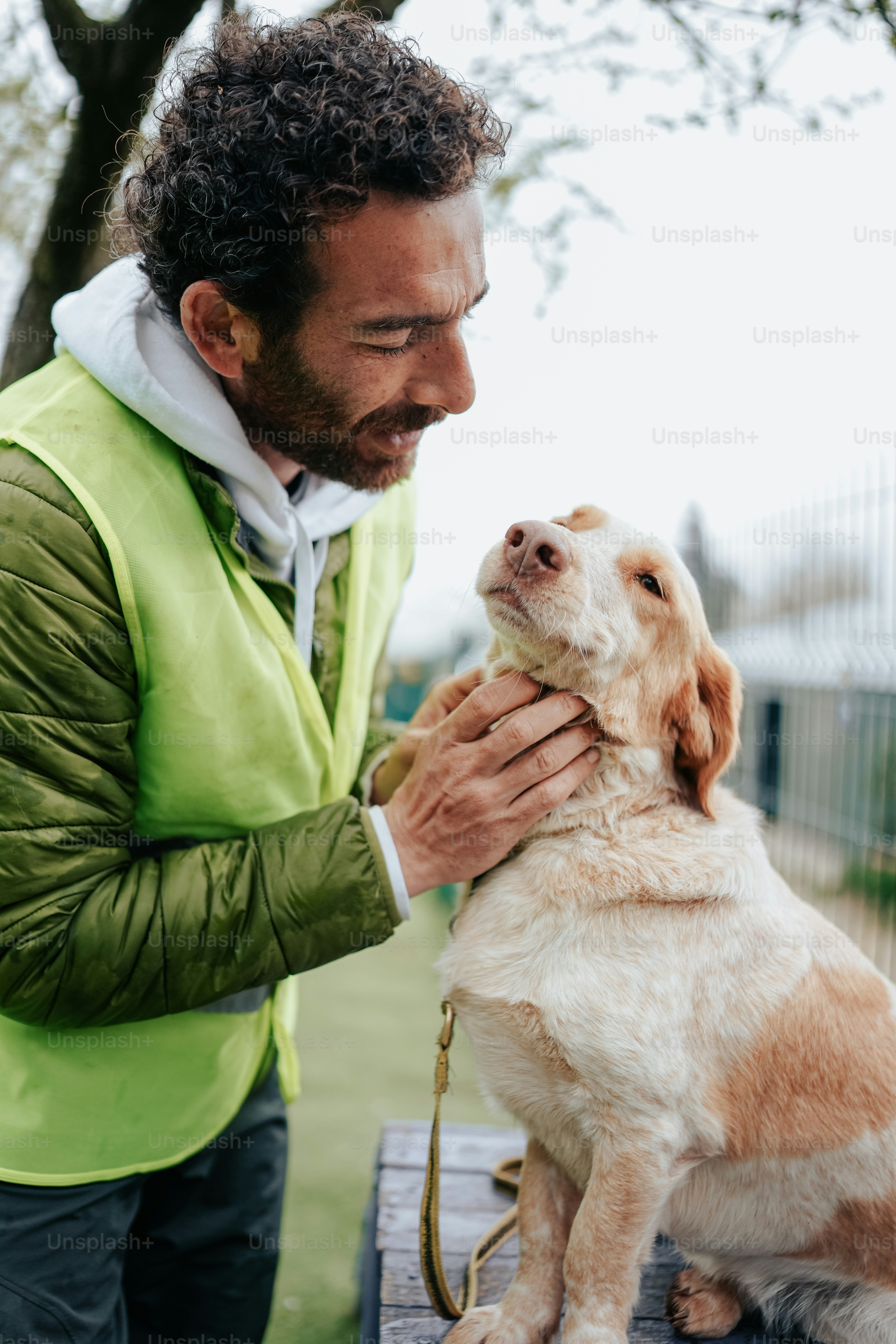 a man in a green jacket petting a brown and white dog