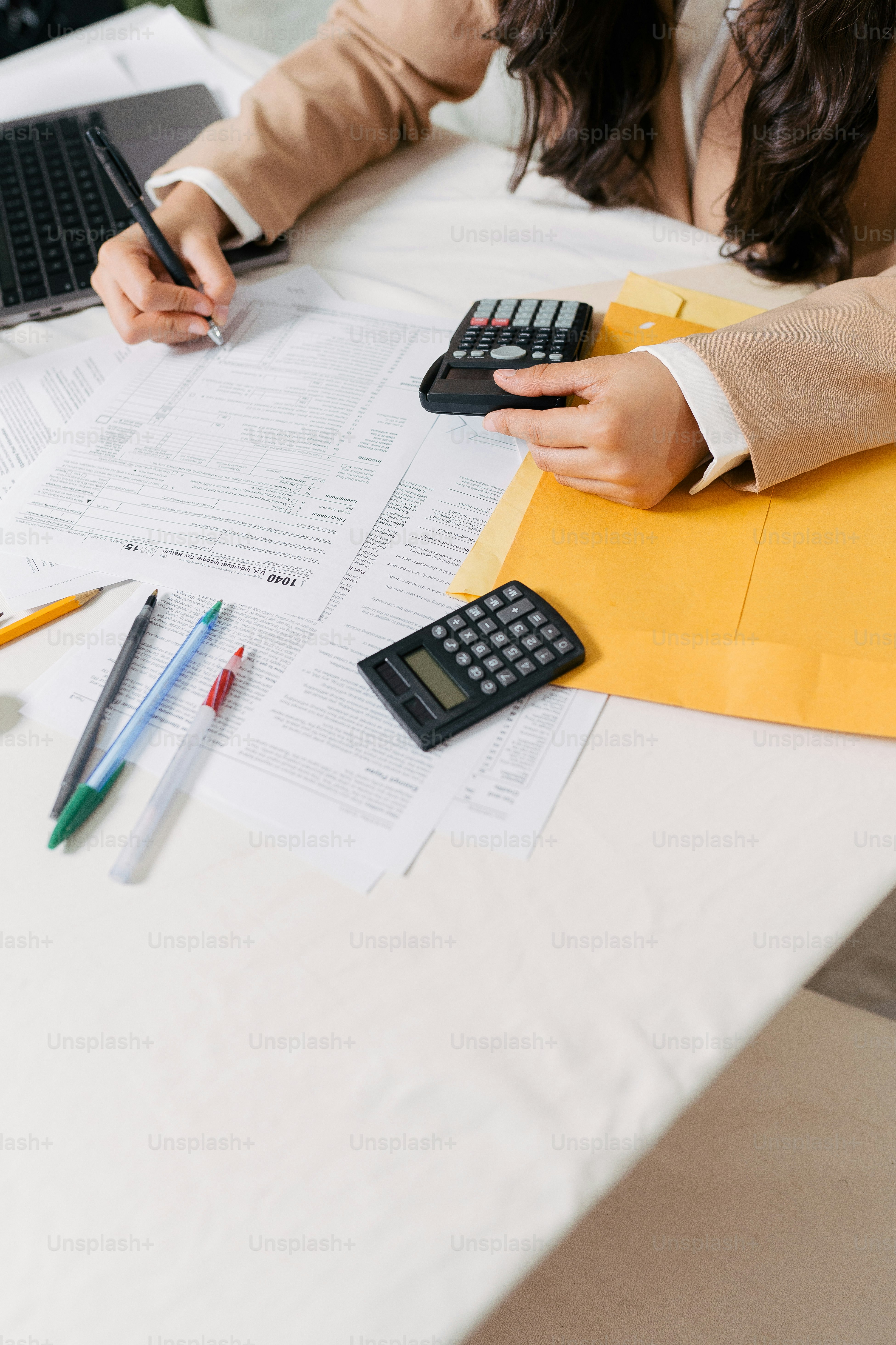 Eine Frau sitzt an einem Tisch mit einem Taschenrechner und einem Laptop