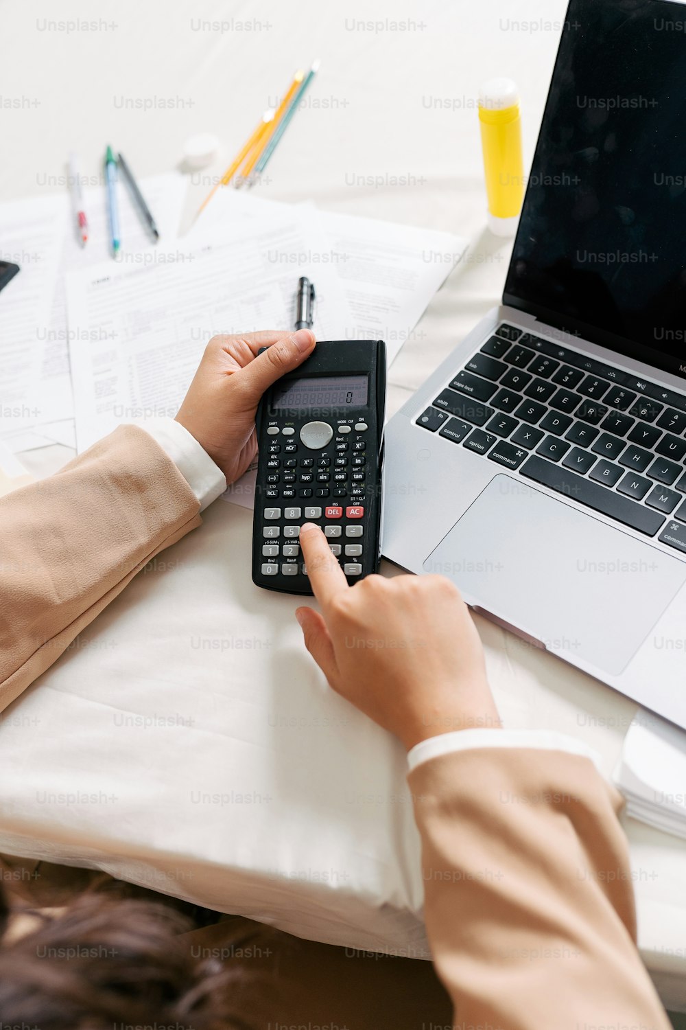 a person sitting at a desk with a calculator and a laptop