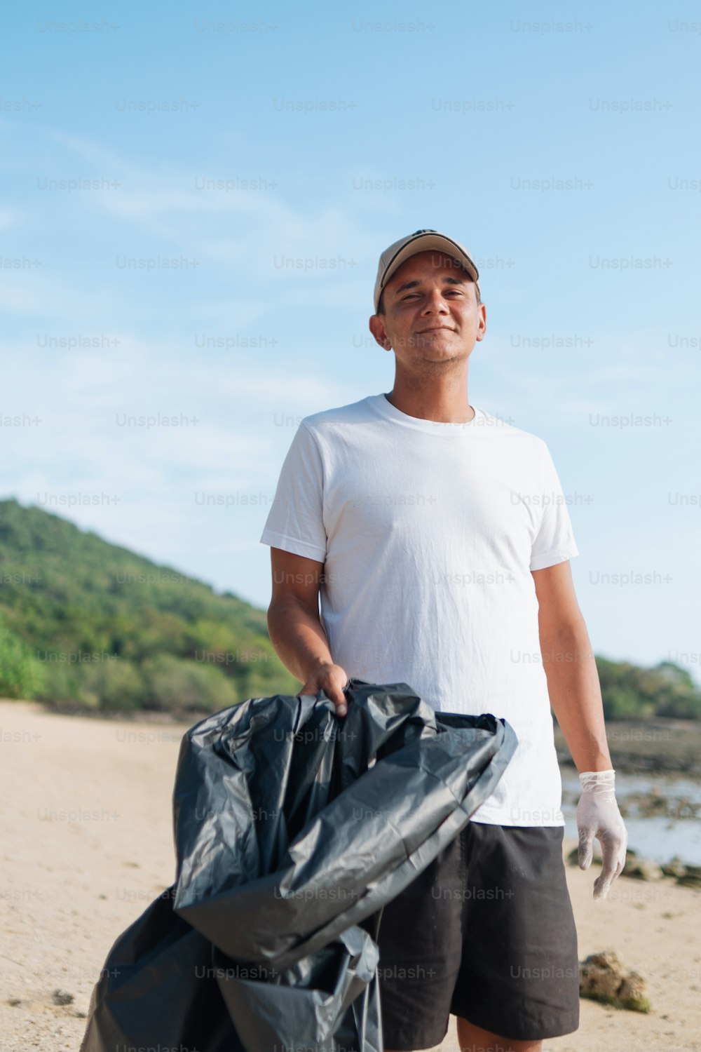 a man standing on a beach holding a bag of garbage