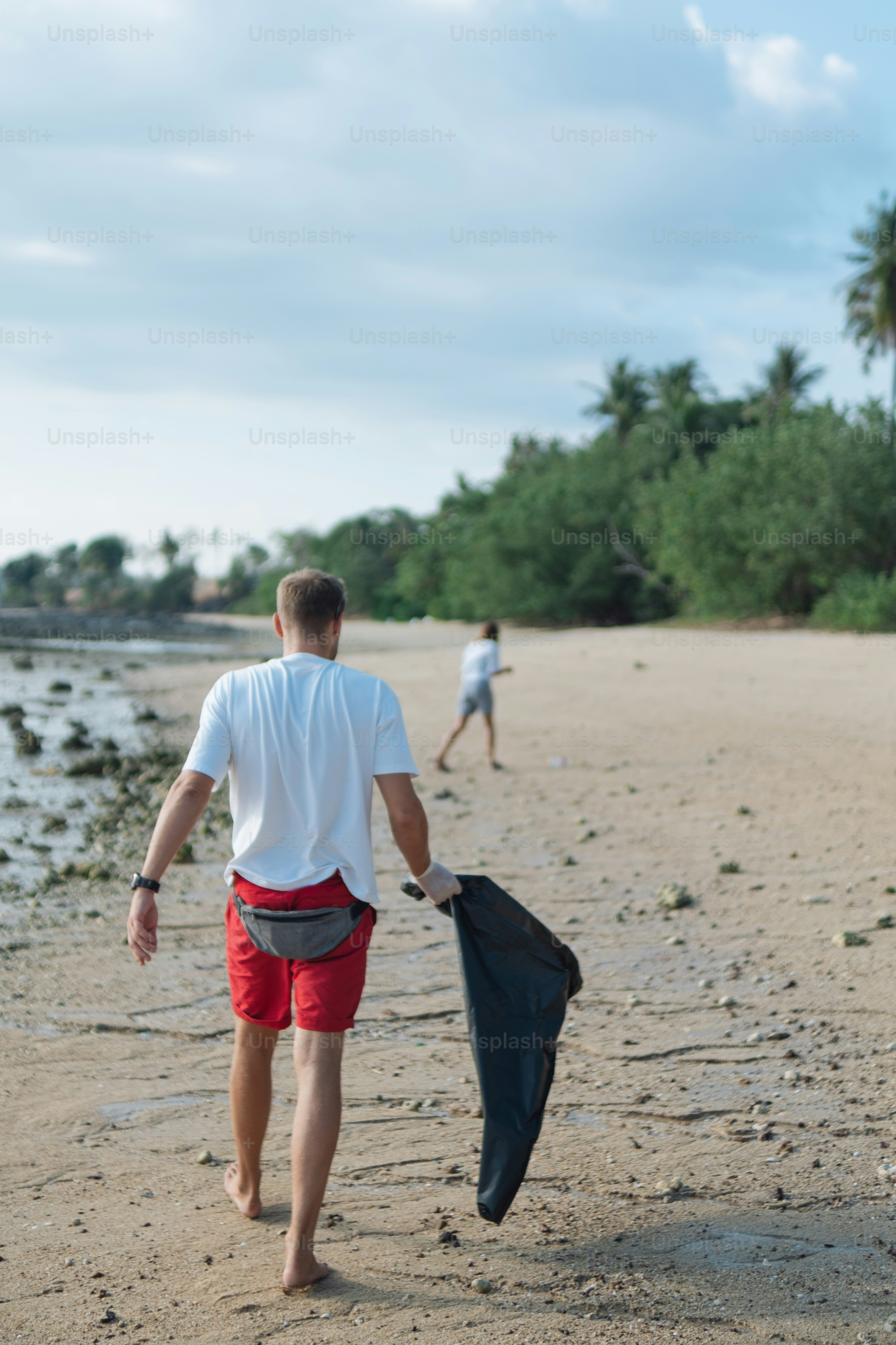 a man walking down a beach carrying a black bag
