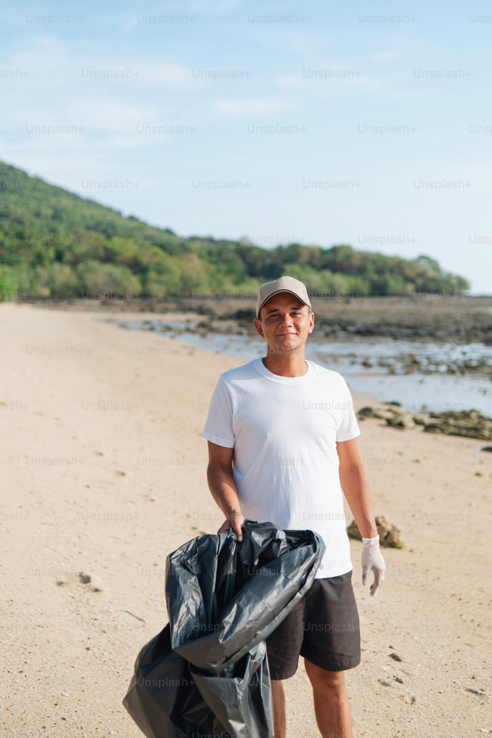 a man standing on a beach holding a bag of garbage