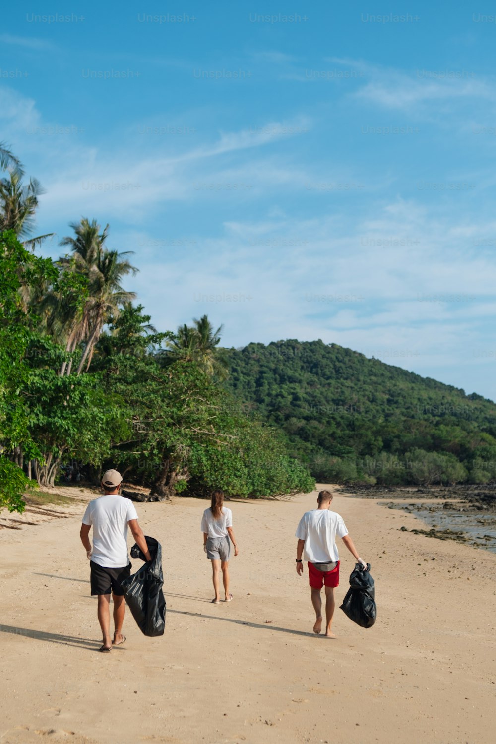 trois personnes marchant sur une plage portant des sacs