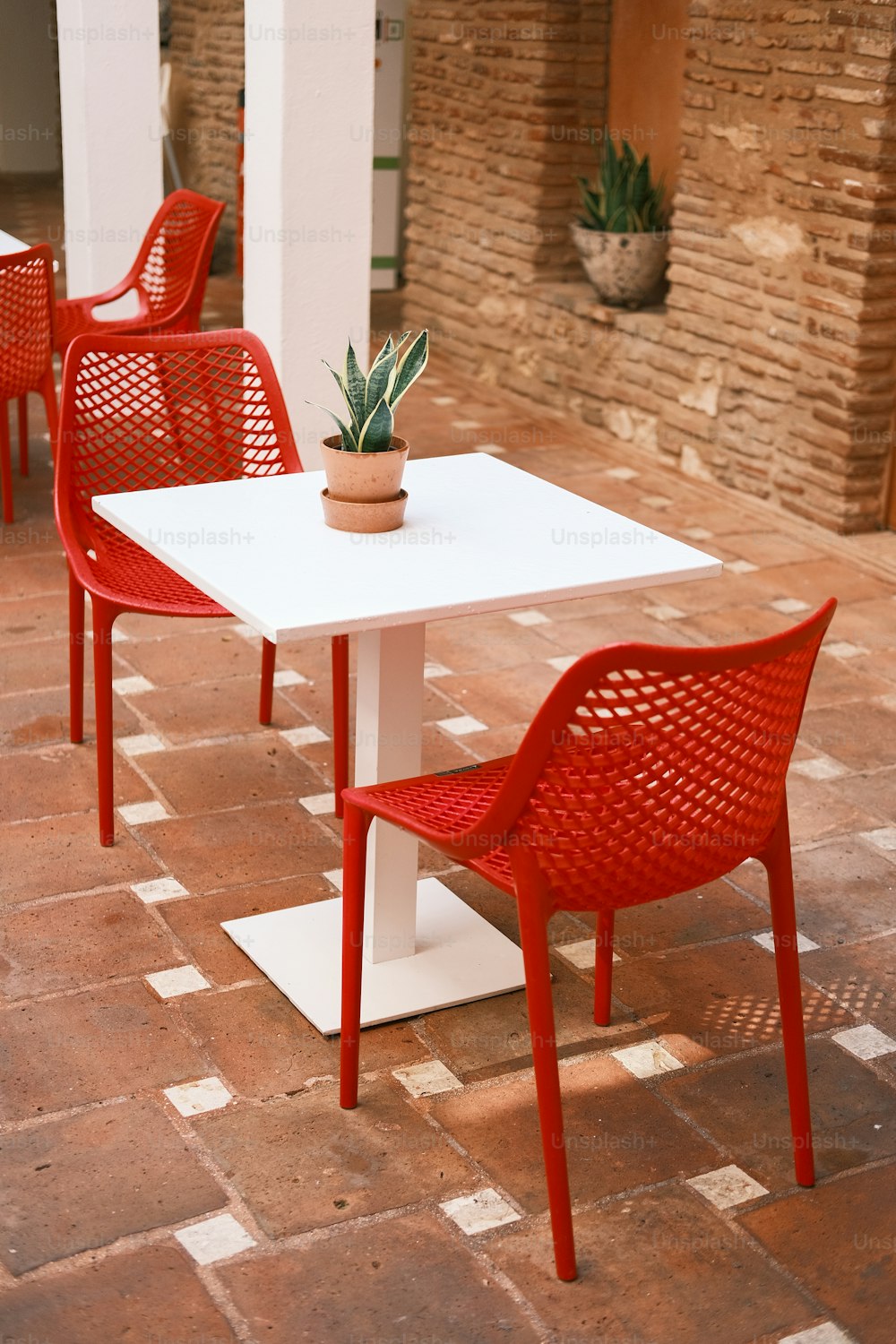 a white table with red chairs and a potted plant