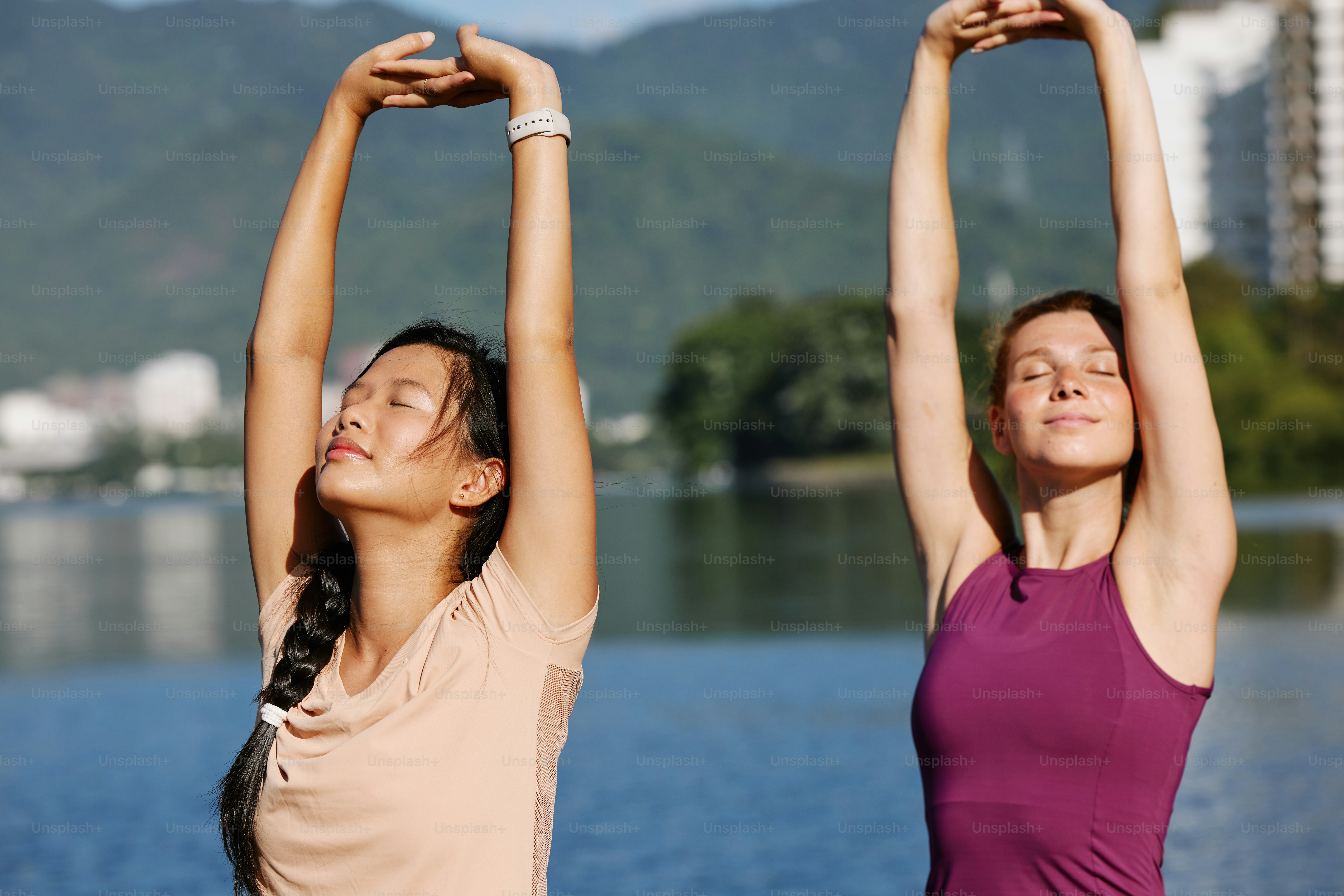 two young women doing yoga exercises by the water