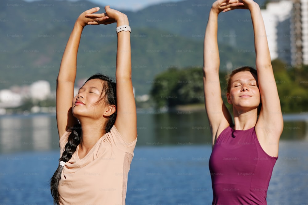 two young women doing yoga exercises by the water