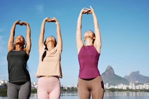 three women doing yoga poses in front of a body of water