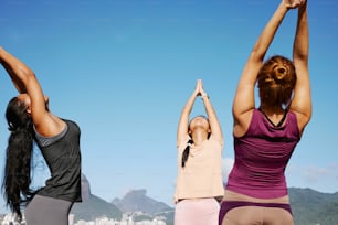 three women doing yoga on a beach with a city in the background