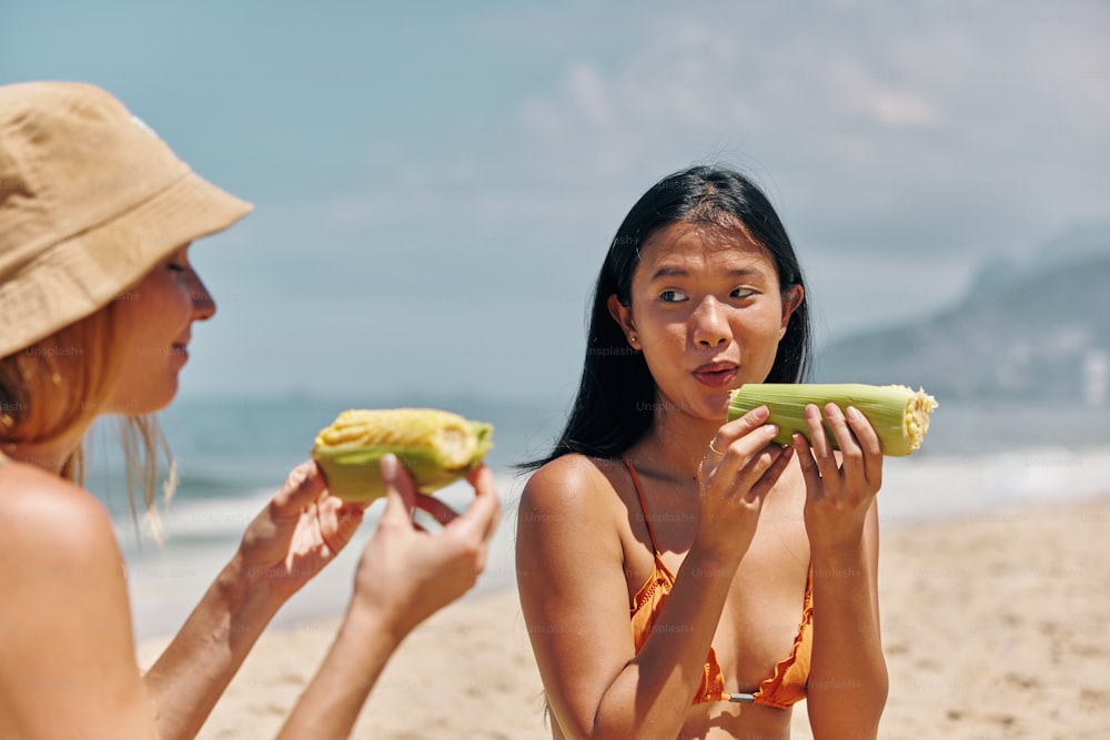 two women sitting on a beach eating food