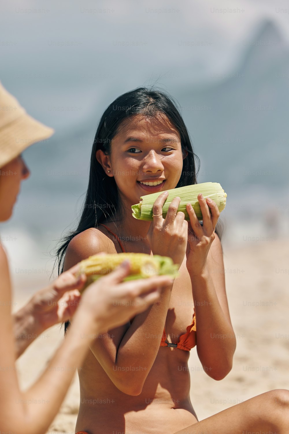 a woman sitting on the beach eating a piece of food